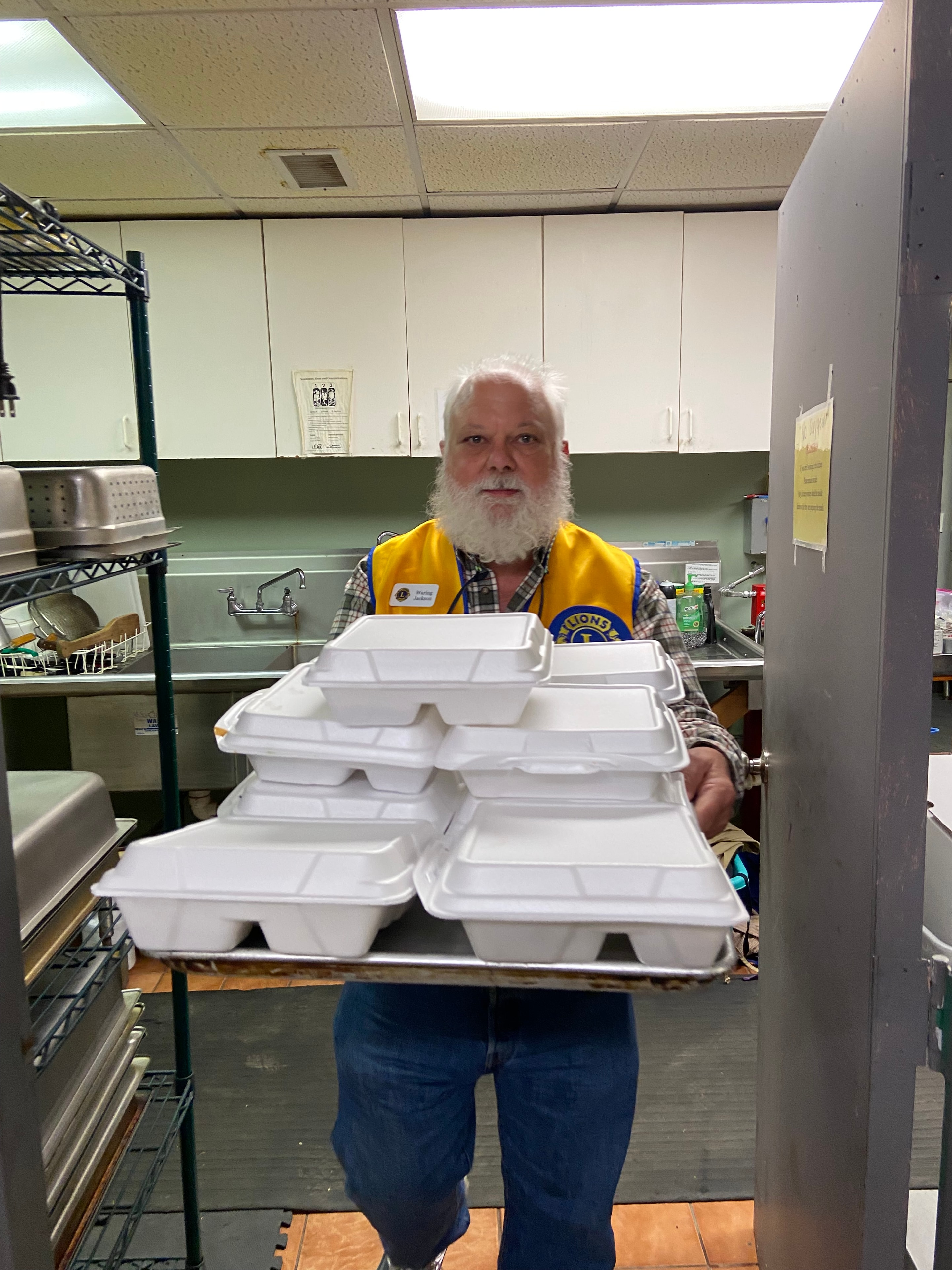 Lions Club member carrying stacked food containers in the kitchen