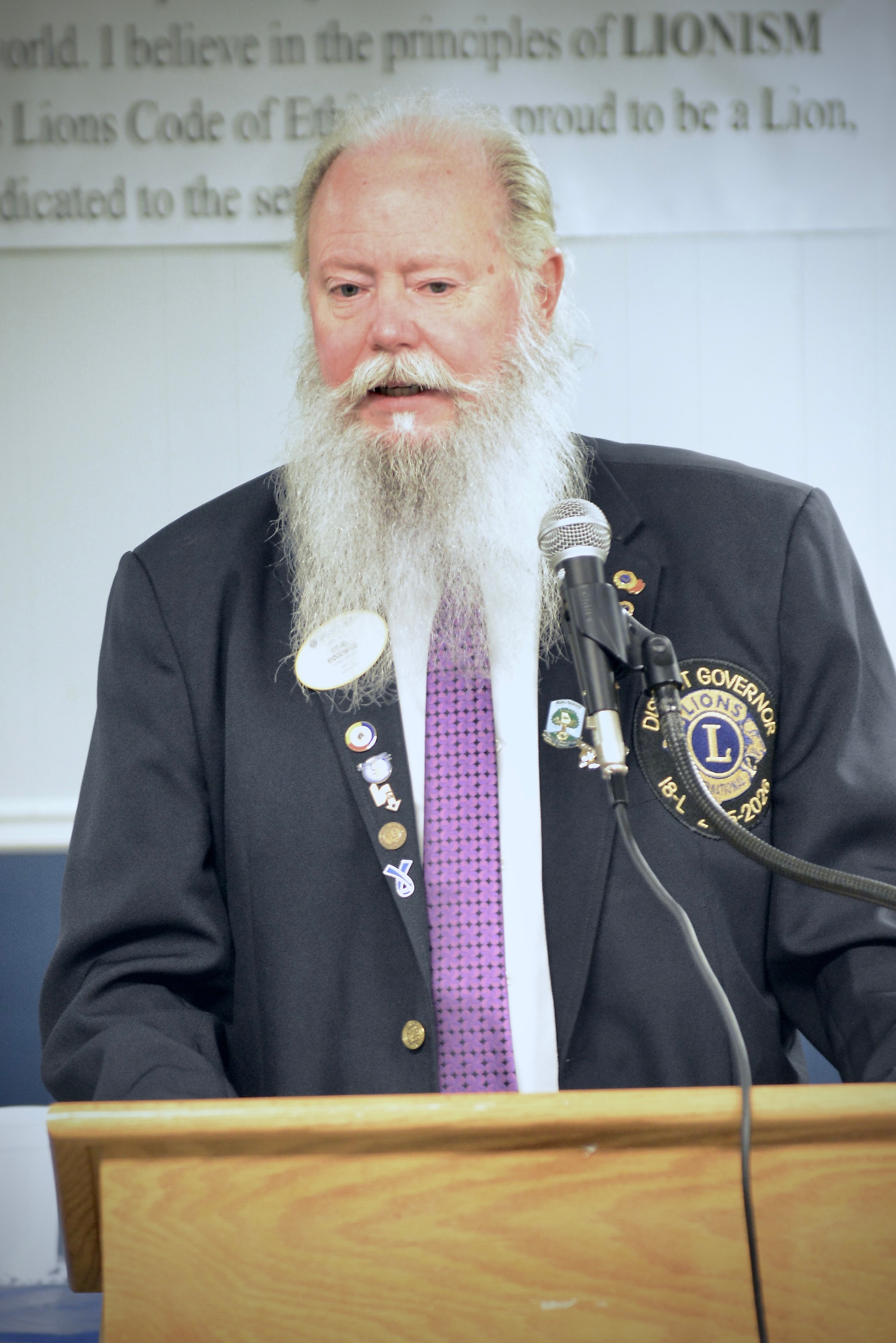 Elderly Lions Club member speaking at the podium during a monthly meeting