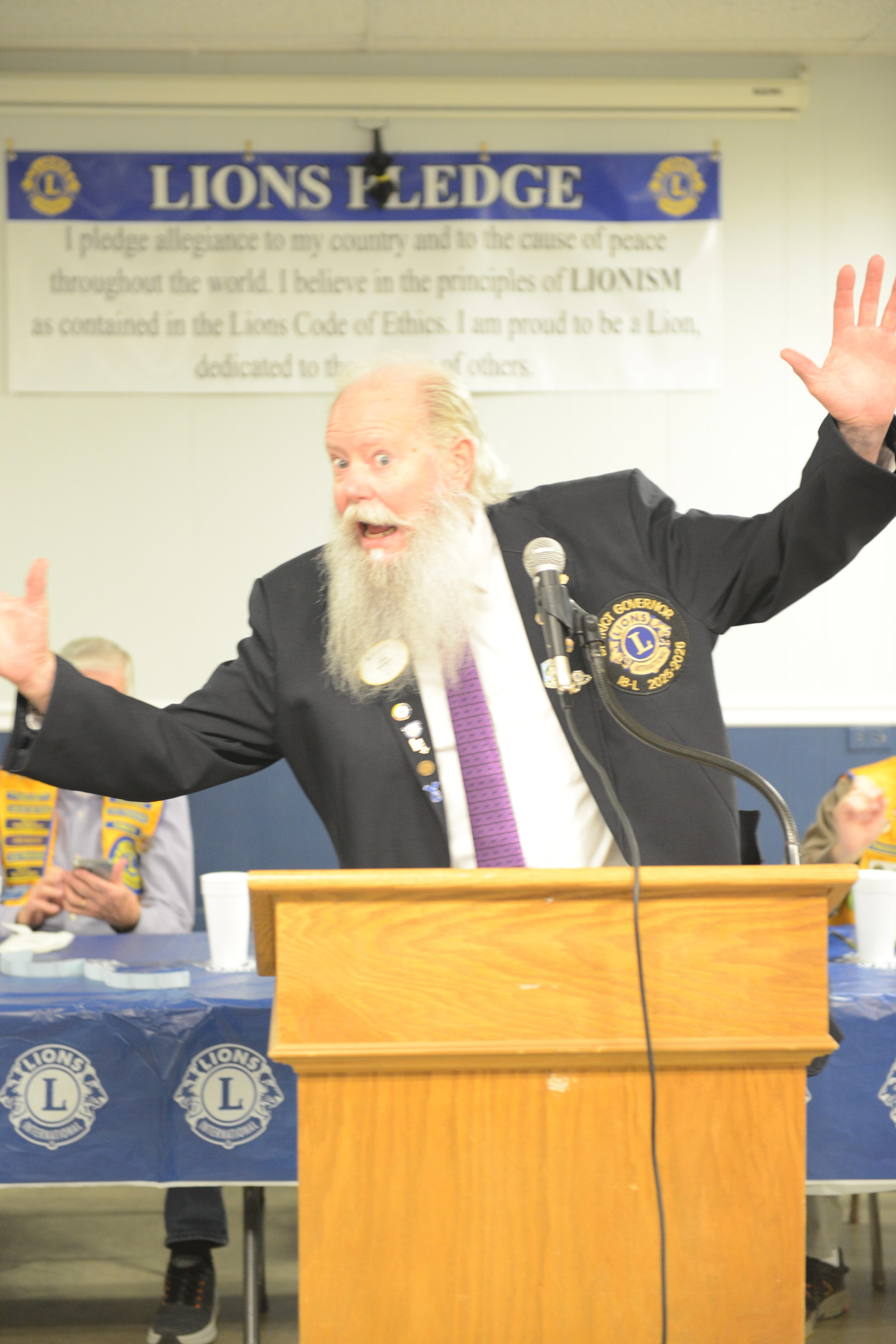 Elderly Lions Club member speaking at the podium during a monthly meeting
