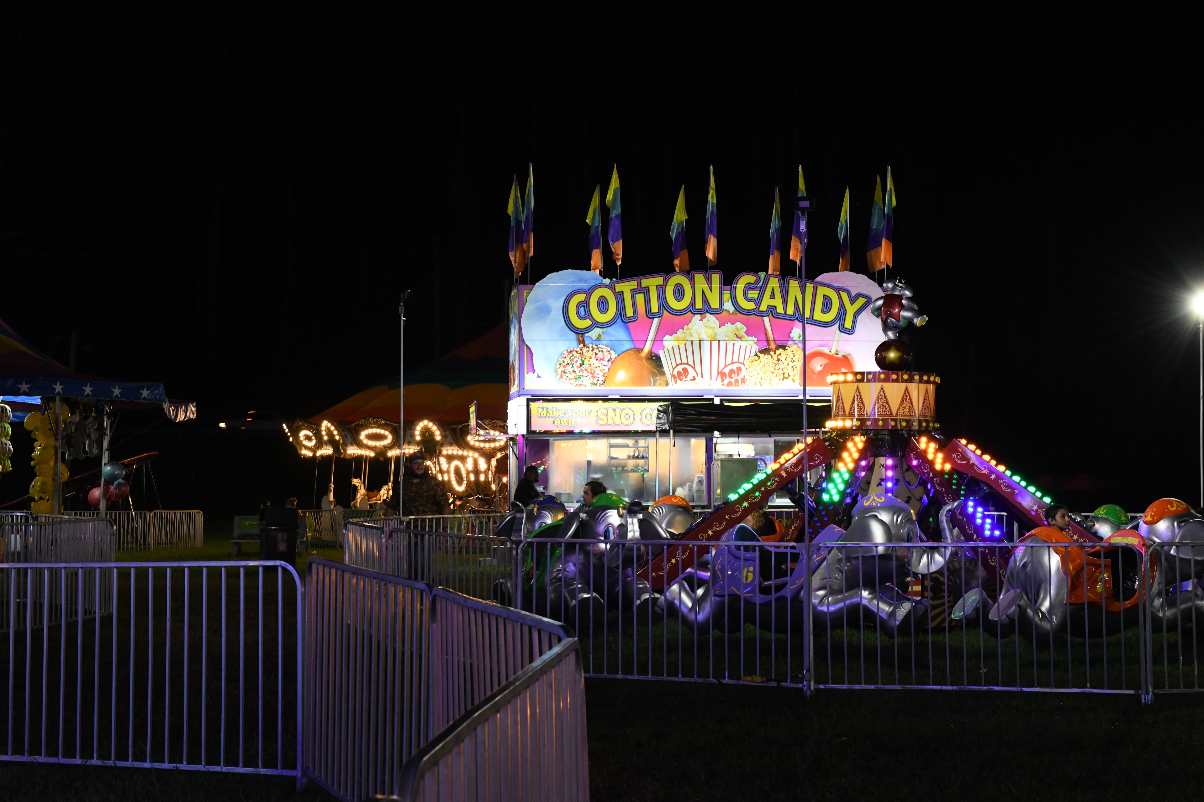 Illuminated carnival cotton candy stand and rides at night at the Gilmer County Fair